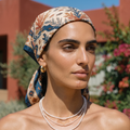 Woman wearing a patterned headscarf and pearl necklace outdoors with blurred background